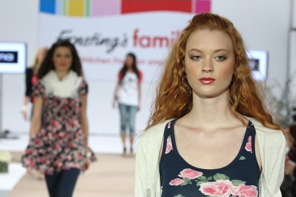 Model mit roten Haaren auf dem Laufsteg, dahinter weitere Models