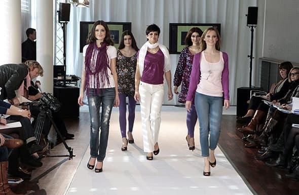 Laufsteg mit fünf Models, seitlich Publikum und Fotografen