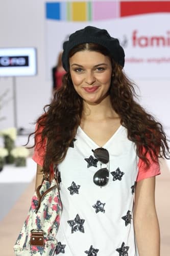 Model mit dunkler Mütze und langen Locken auf dem Laufsteg