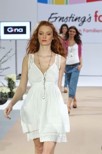 Model im weissen Kleid mit langen roten Haaren auf dem Laufsteg