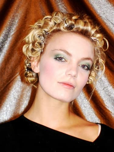 Model mit Lockenfrisur und farbigem Lidschatten vor glänzendem Hintergrund