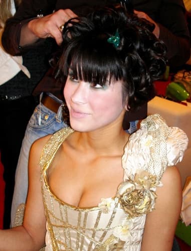 Backstage: Model mit gelockter Hochsteckfrisur und Corsage, eine Hand richtet das Haar